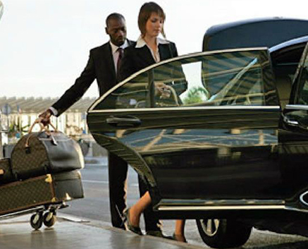 Businesswoman entering a car with a chauffeur holding luggage.