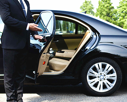A chauffeur opening a luxury car door with a key in hand.