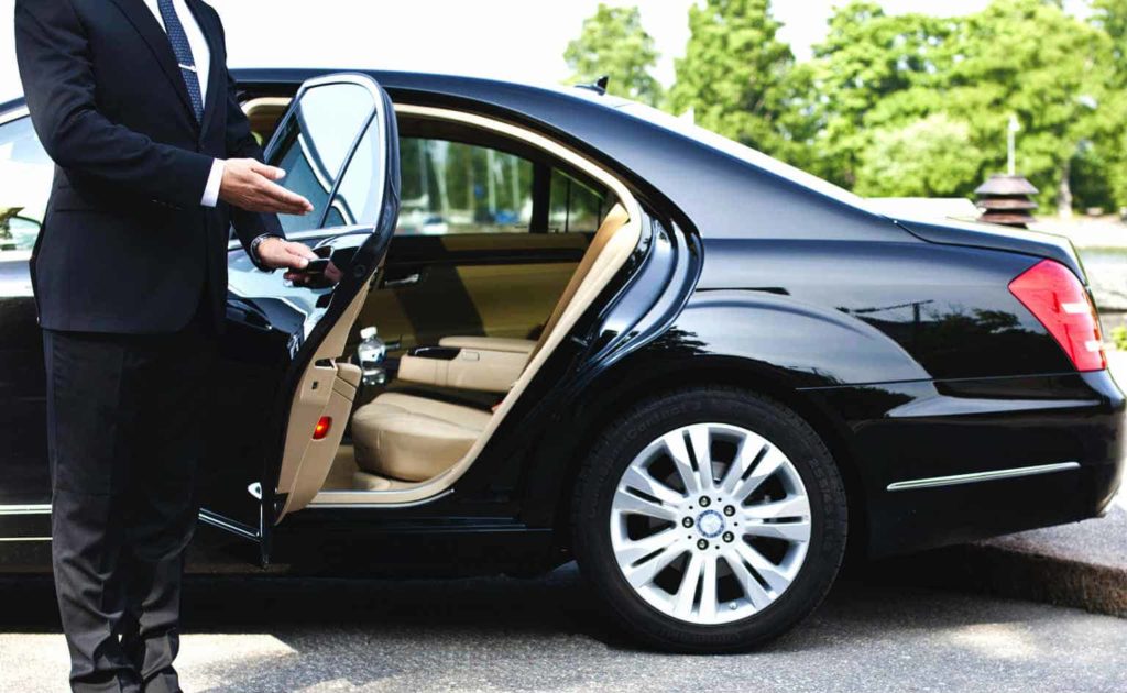 A person opening the rear door of a black luxury car.