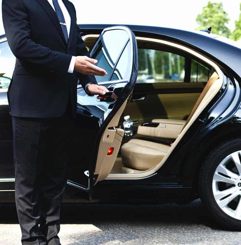 A chauffeur opens the car door for a passenger.