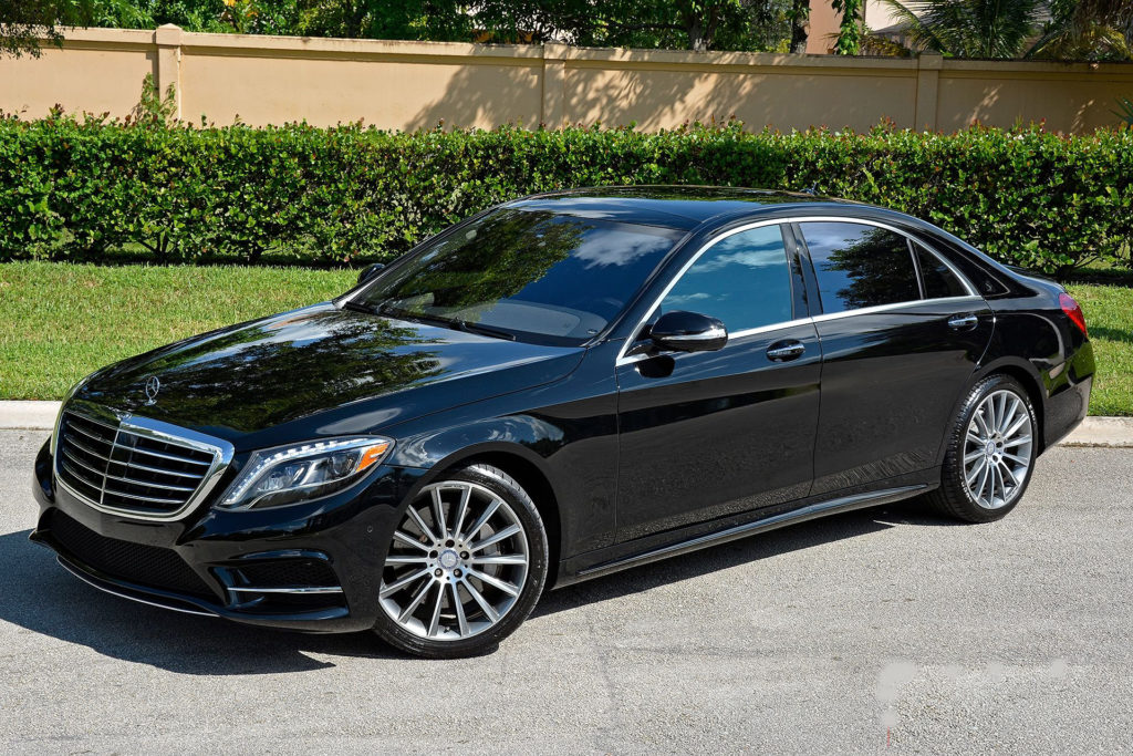 A sleek black luxury sedan parked on a sunny driveway.