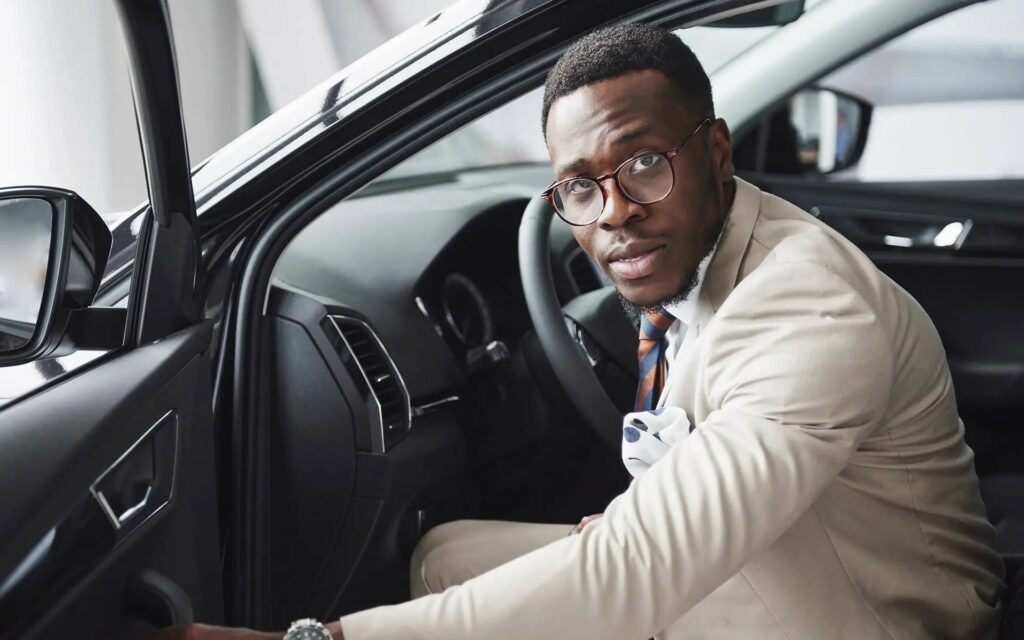 Man sitting in car driver's seat, smiling.
