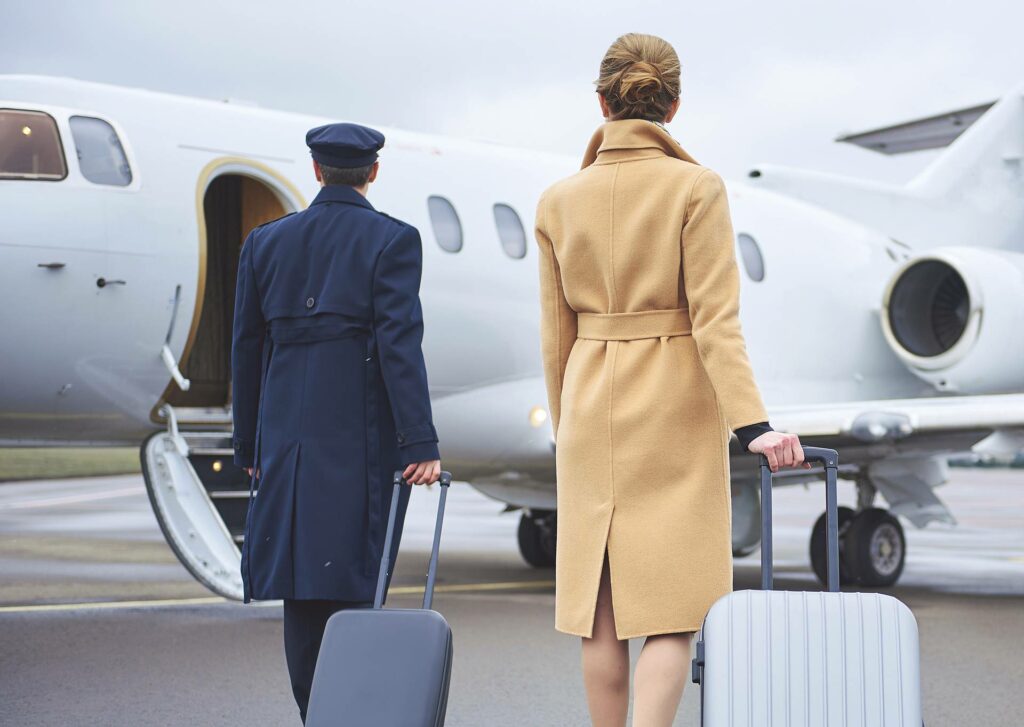 Two travelers walking towards a private jet with luggage.